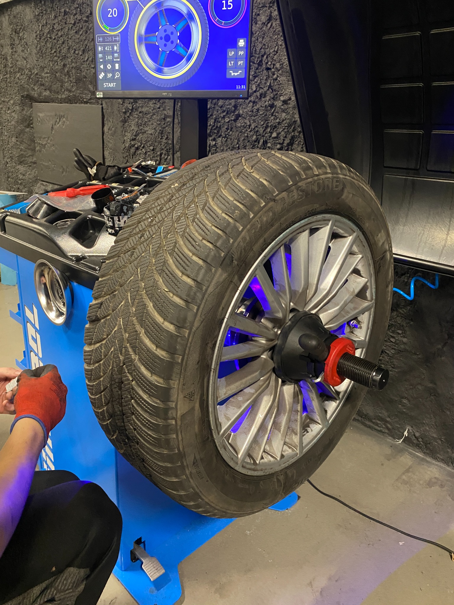 Wyważanie koła zimowego Bridgestone na maszynie z podświetleniem LED i ekranem diagnostycznym w warsztacie.