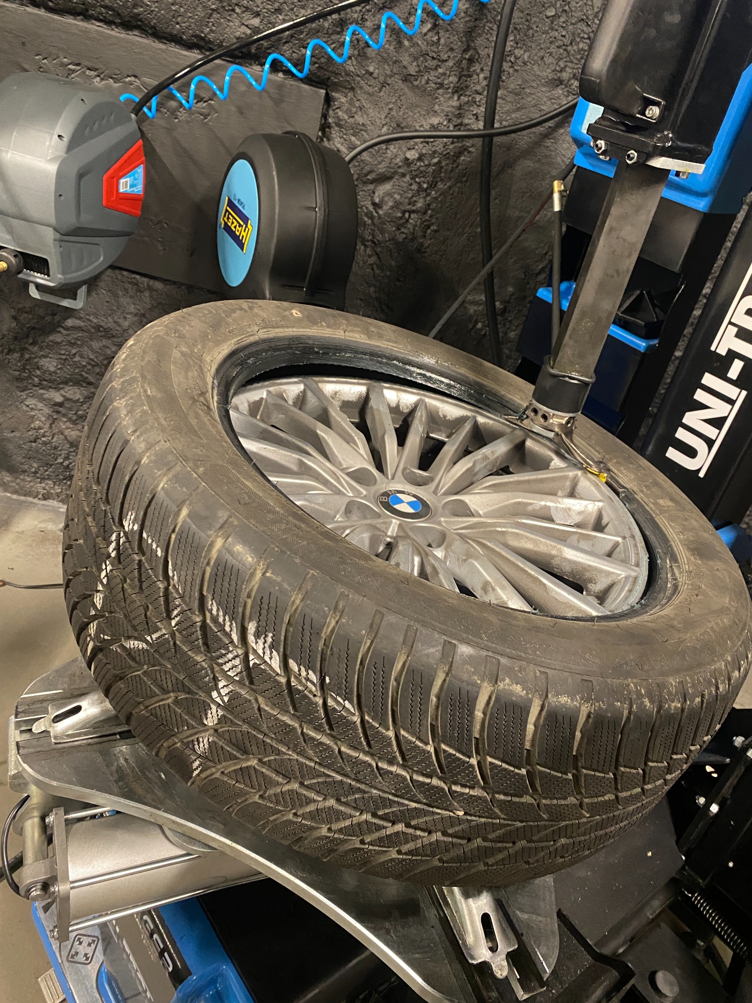 Opona zimowa BMW na montażownicy UNI-TROLL, widoczne ślady po kredzie na bieżniku, szara felga aluminiowa.