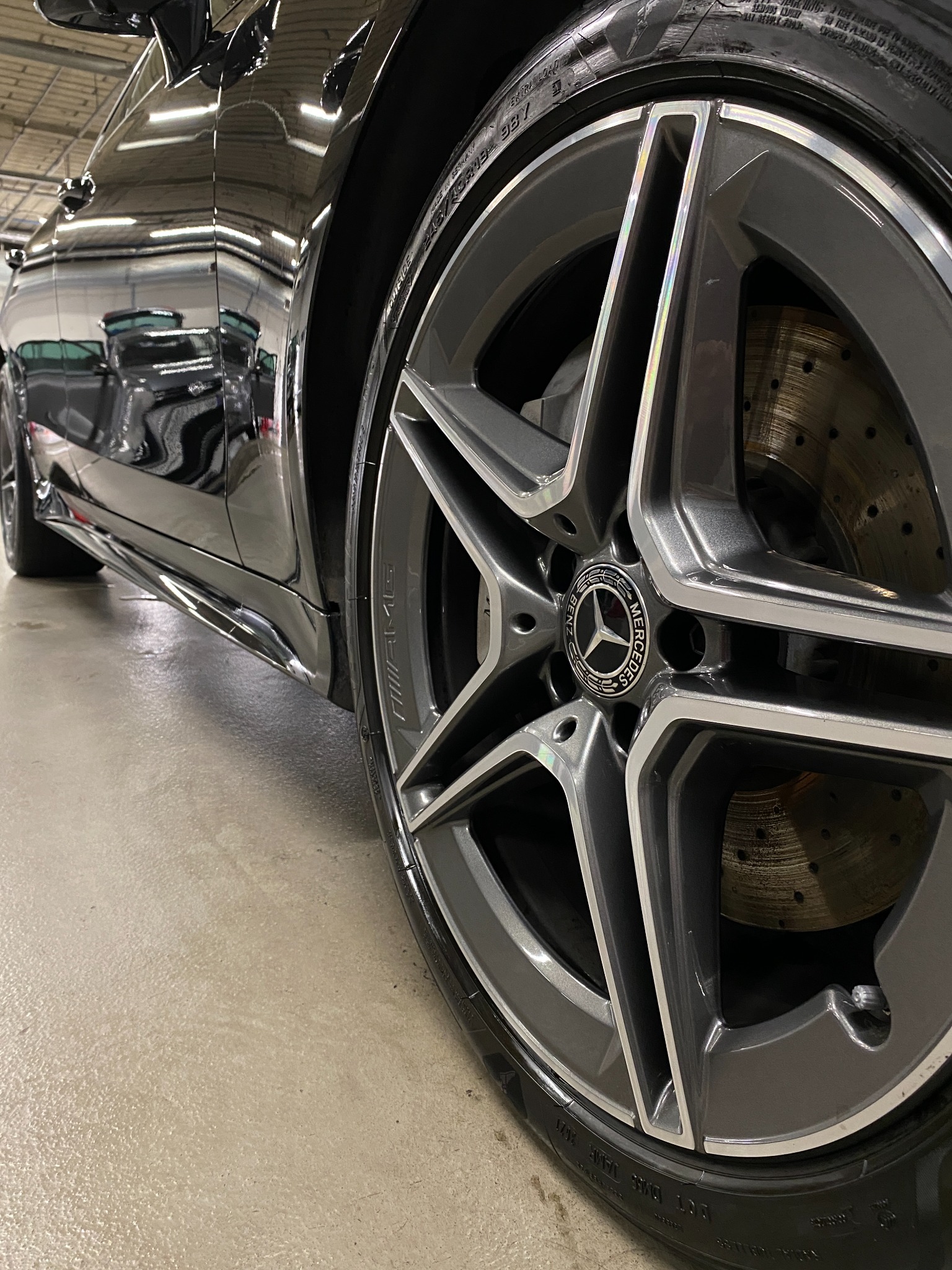 Błyszczące, czarne nadwozie samochodu marki Mercedes-Benz z widocznym aluminiowym felgi AMG z pięcioramiennym wzorem, po zabiegu pielęgnacyjnym w myjni.