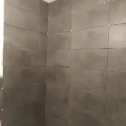 Świeżo ułożone, ciemnoszare płytki w łazience, z krzyżykami dystansowymi w spoinach, dolna krawędź przy wannie jeszcze niezafugowana.