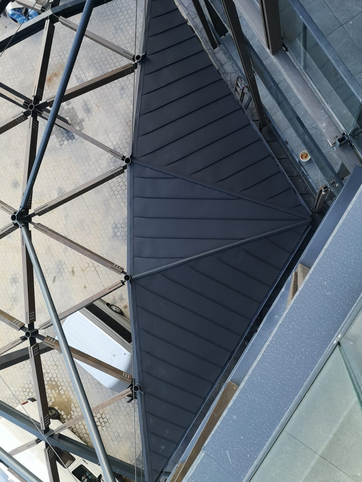 Nowoczesna konstrukcja dachu z blachy na budynku, widok z góry, z elementami szklanymi i kostką brukową w tle. Metalowa konstrukcja nośna.