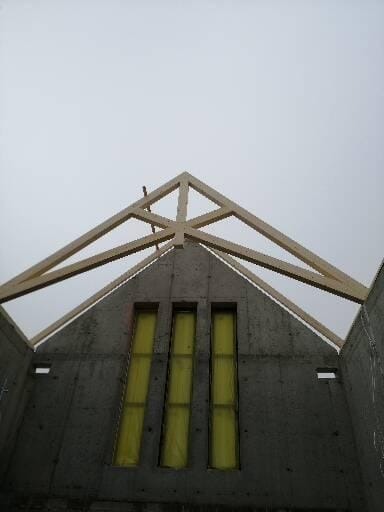 Surowy stan dachu z drewnianą konstrukcją i trzema oknami z żółtą folią w szarym betonie. Widok z dołu na niebo.