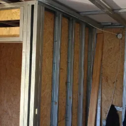 Konstrukcja ścian działowych z profili stalowych i płyt OSB w trakcie budowy, widoczne instalacje elektryczne i hydrauliczne.