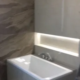 Nowoczesna wanna obudowana płytkami, z podświetlaną wnęką na ścianie w wykończonej łazience.