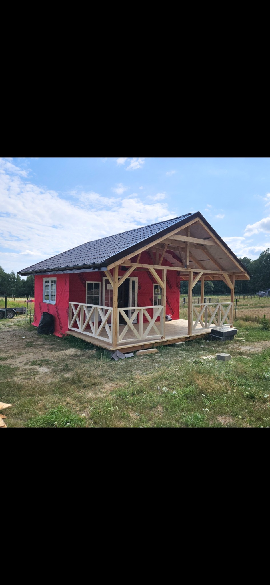 Budowa domu szkieletowego w Miliczu. Widoczna konstrukcja dachu, ściany pokryte membraną, drewniany taras z balustradą. Etap przed ociepleniem i wykończeniem elewacji.