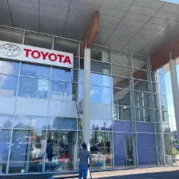 Pracownik z użyciem długiej lancy myje przeszkloną fasadę salonu samochodowego Toyota w Babicach, widoczne odbicia w szybach.