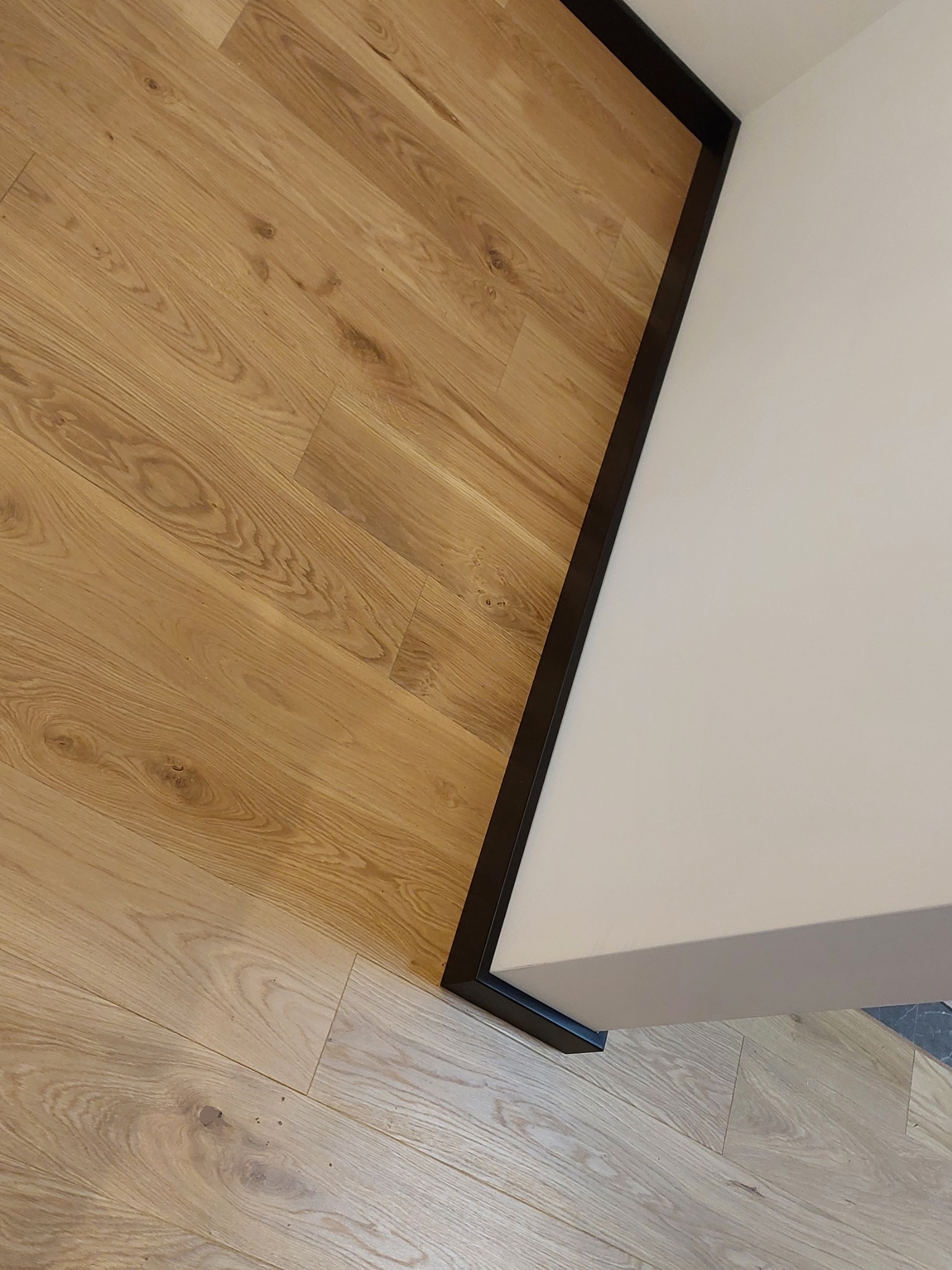 Jasny parkiet ułożony przy białej ścianie z czarną listwą przypodłogową.