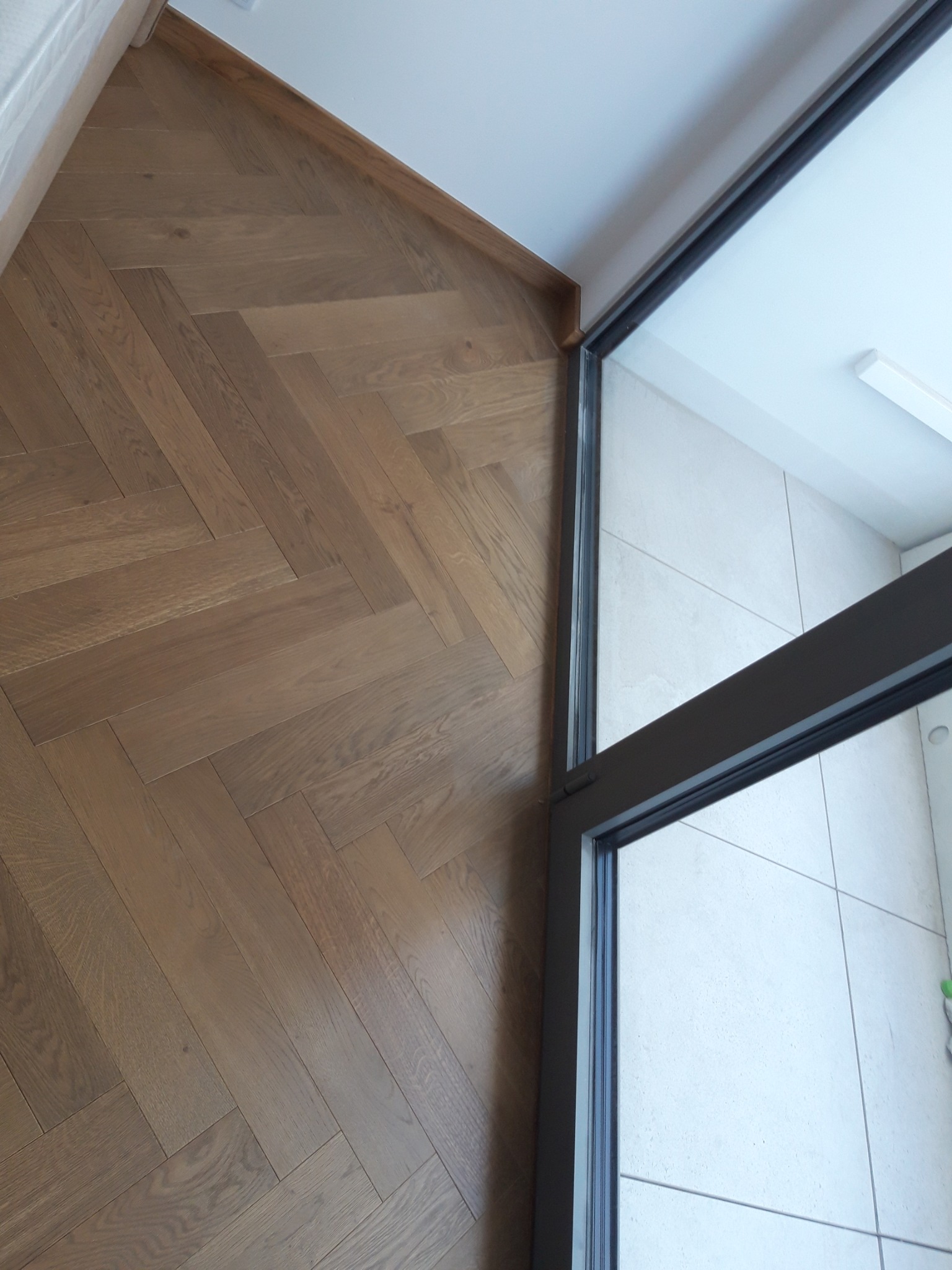 Ułożony parkiet w jodełkę francuską z widocznym progiem drzwiowym i fragmentem ściany.