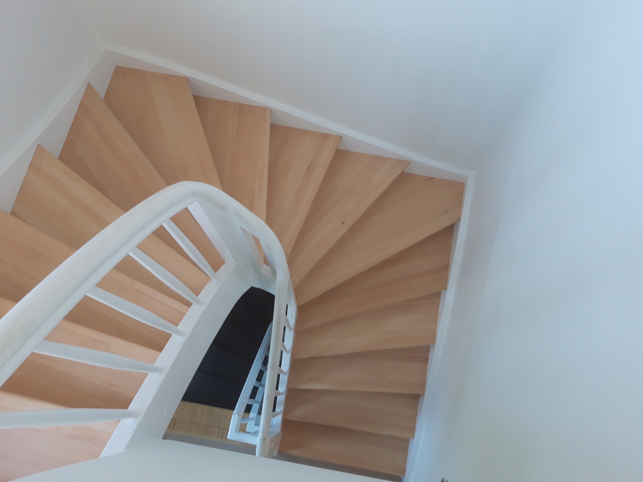 Widok z góry na drewniane, spiralne schody z białymi balustradami w jasnym wnętrzu.