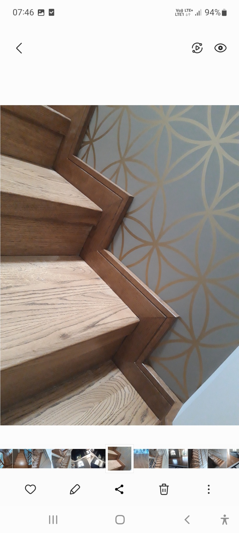 Jasne, drewniane schody z ozdobną listwą przypodłogową, na tle ściany z geometrycznym wzorem w kolorze złota.