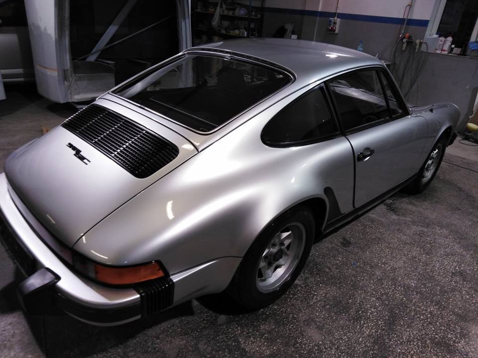 Srebrny samochód sportowy Porsche 911, widok z tyłu w warsztacie, z widocznymi elementami karoserii i oświetleniem warsztatowym.