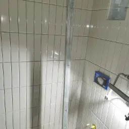 Ściany łazienki wyłożone pionowymi, białymi płytkami w trakcie remontu, widoczny metalowy profil, puszka podtynkową i elementy instalacji wodnej.