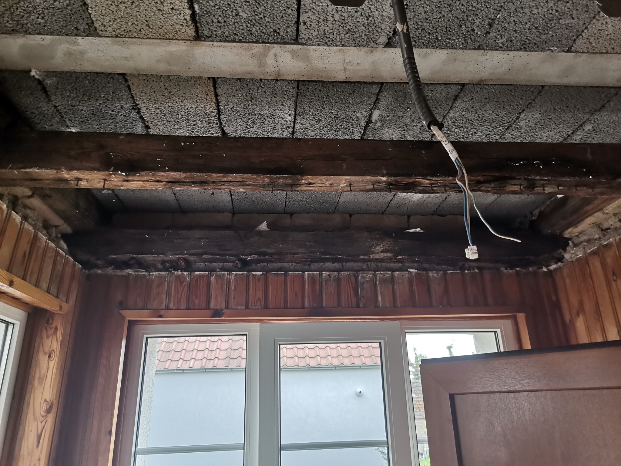 Poddasze przed ociepleniem: widoczne bloczki betonowe, drewniana konstrukcja stropu, wystające przewody elektryczne, boazeria i okno.