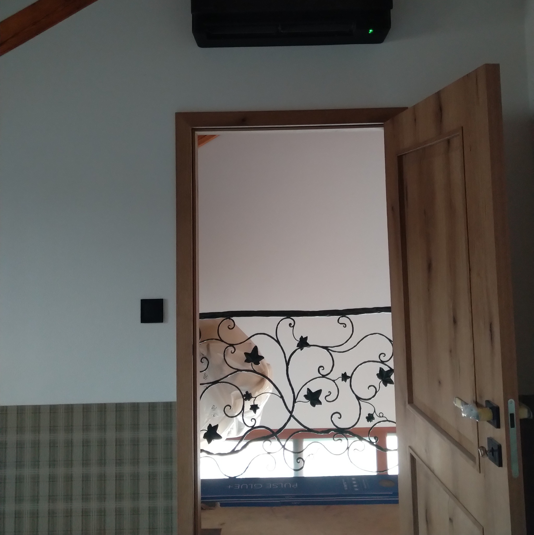 Otwarta drewniana dębowa  brama z ozdobną balustradą w tle, klimatyzator na ścianie, widok z dołu.