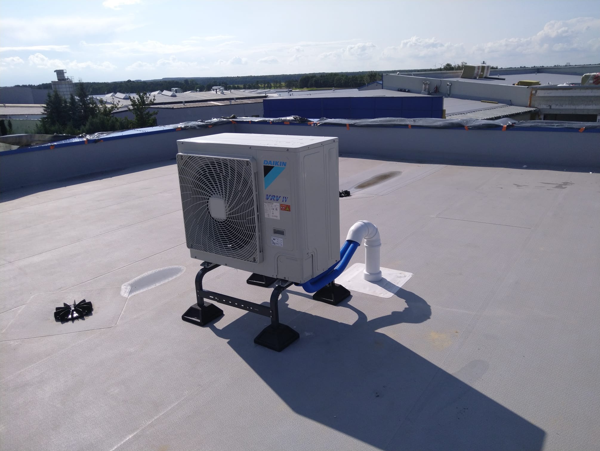 Klimatyzator Daikin VRV IV na dachu budynku komercyjnego, z widocznymi elementami instalacji i tłem miejskiego krajobrazu. Ujęcie z góry, w słoneczny dzień.