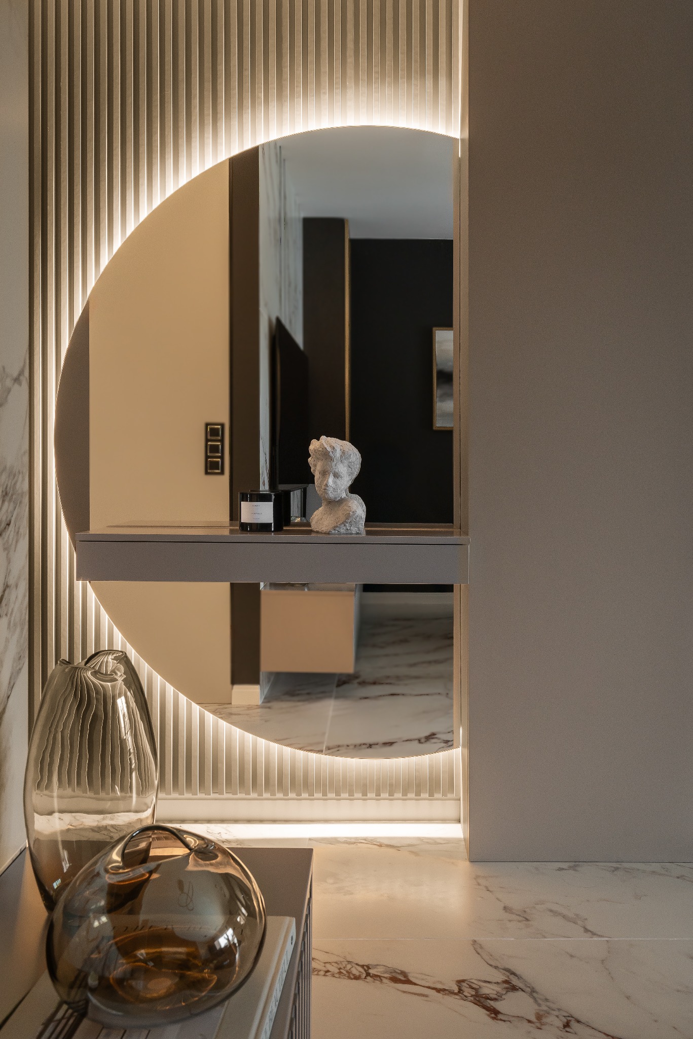 Nowoczesne wnętrze z okrągłym lustrem podświetlonym LED, marmurowa podłoga, dekoracyjne wazony i rzeźba popiersia. Minimalistyczny design, ciepłe oświetlenie akcentujące.