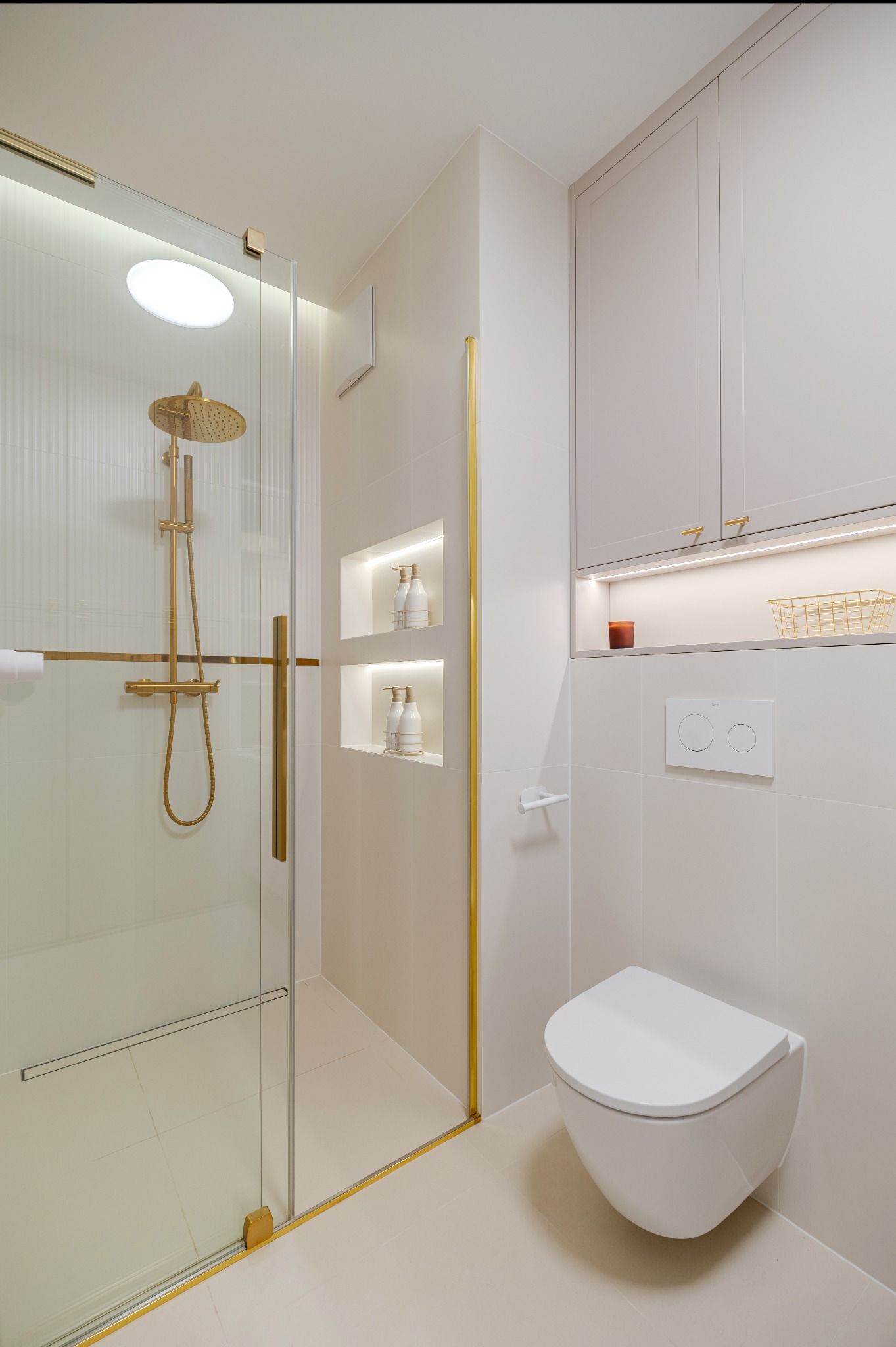 Elegancka łazienka w Warszawie po remoncie. Kabina prysznicowa ze złotymi detalami, wnęki z oświetleniem i minimalistyczna toaleta podwieszana.