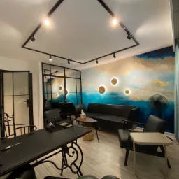 Nowoczesne biuro z czarnymi meblami, ozdobną ścianą z motywem nieba i złotymi akcentami, oświetleniem szynowym i dekoracyjnym zegarem ściennym.