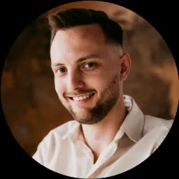 Portret uśmiechniętego mężczyzny z krótką brodą i modną fryzurą w koszuli na rozmytym tle.