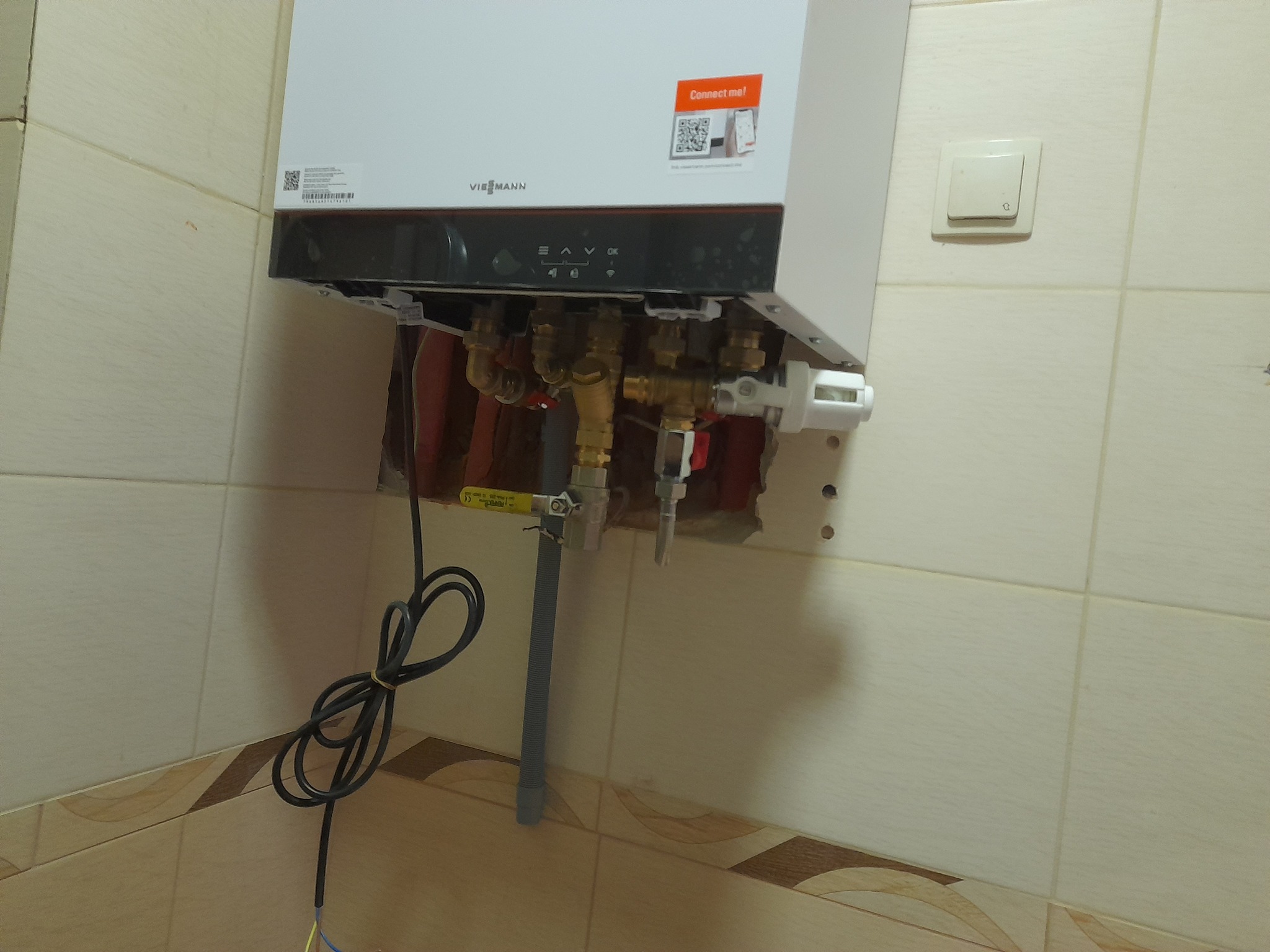 Nowy piec gazowy Viessmann, zamontowany na kafelkowanej ścianie, widoczne przyłącza hydrauliczne i przewód zasilający