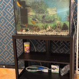 Ślusarstwo-Spawalnictwo Artem Sidorenko - Czarny metalowy stojak pod akwarium z rybami, na półkach karma dla ryb i akcesoria do czyszczenia.