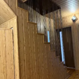 Schody drewniane z nietypową pionową konstrukcją zabezpieczającą, drewniane panele ścienne i sufitowe, widoczny fragment podłogi z wzorem geometrycznym.