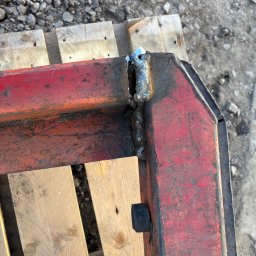 Ślusarstwo-Spawalnictwo Artem Sidorenko - Czerwona, metalowa rama z widocznym spoiwem na rogu, leżąca na drewnianej palecie, z kamienistym podłożem w tle.