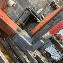 Ślusarstwo-Spawalnictwo Artem Sidorenko - Spoina łącząca dwa metalowe profile pod kątem prostym, widoczne ślady po spawaniu, fragment konstrukcji z profili pomalowanych na pomarańczowo i czarno, w tle narzędzia warsztatowe.