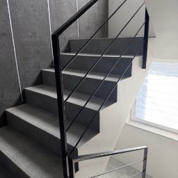 Ślusarstwo-Spawalnictwo Artem Sidorenko - Nowoczesne schody z czarną, metalową konstrukcją i szarymi stopniami, oświetlone naturalnym światłem z okna. Minimalistyczny design z akcentem na geometrię.