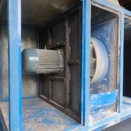 Wnętrze przemysłowej instalacji wentylacyjnej z wentylatorem i silnikiem elektrycznym, widoczne elementy konstrukcji stalowej pomalowanej na niebiesko, zakurzone powierzchnie.