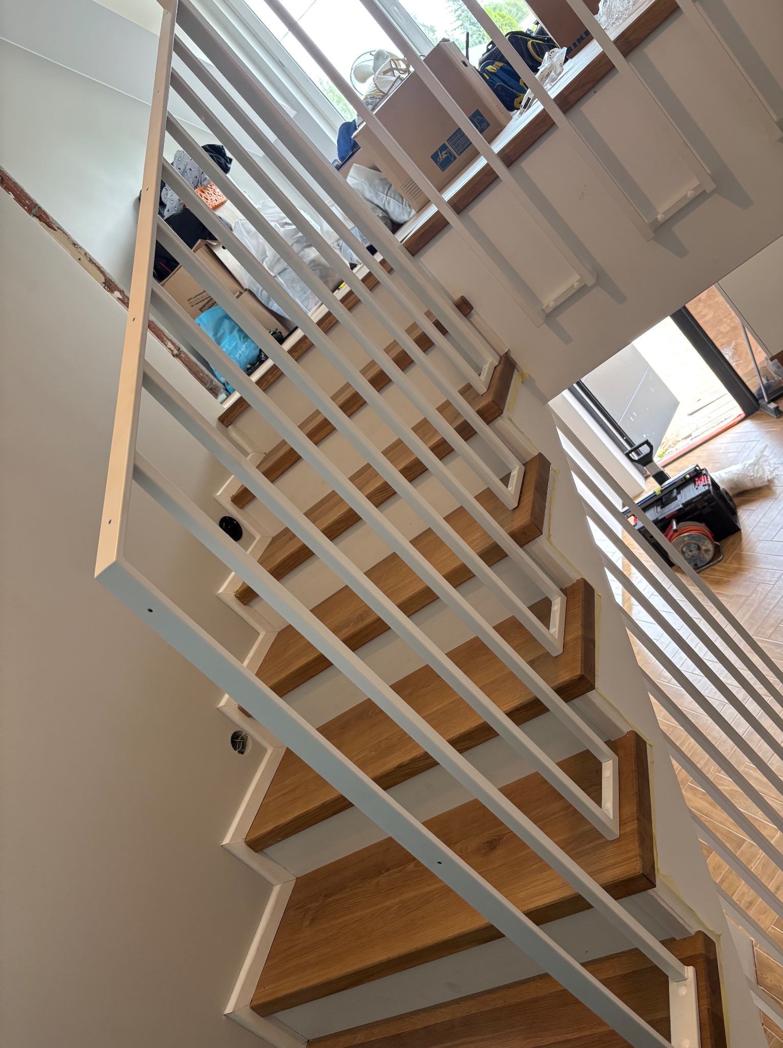 Nowoczesne schody z drewnianymi stopniami i białymi, prostymi barierkami. Widok z góry, z narzędziami w tle, sugerujący montaż.