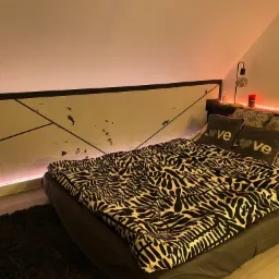 Pokój na poddaszu z łóżkiem, oświetleniem LED, ścianą z geometrycznym wzorem i dekoracyjnymi poduszkami z napisem 'LOVE'.