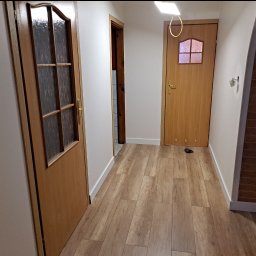 JKM Renovation Jakub Mrzygłód - Korytarz z trzema drewnianymi drzwiami, parkietem i łukiem z cegły, widok na wnętrze mieszkania.