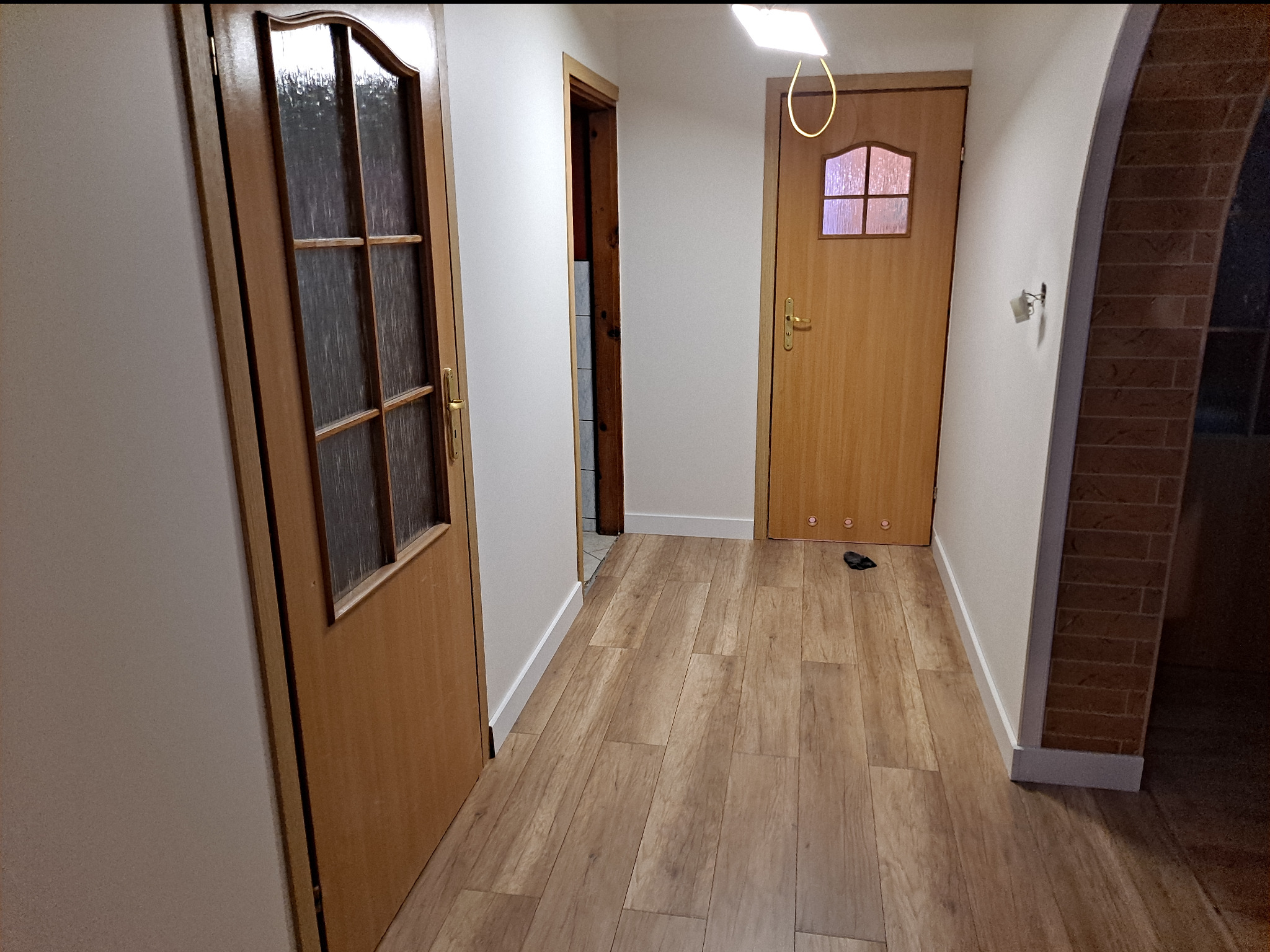 Korytarz z trzema drewnianymi drzwiami, parkietem i łukiem z cegły, widok na wnętrze mieszkania.