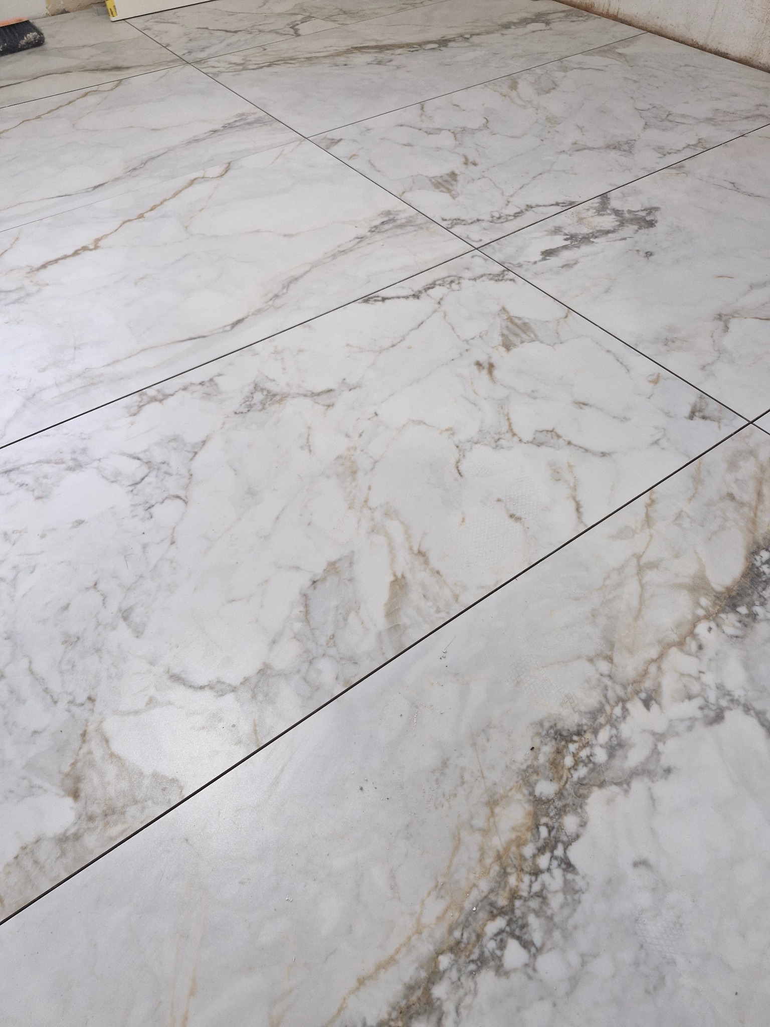 Ułożona podłoga z płytek imitujących marmur w odcieniach bieli, szarości i złota, z widocznymi fugami w kolorze ciemnoszarym.