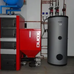 Nowoczesny, automatyczny piec na paliwo stałe DUOX z podajnikiem, zbiornikiem na paliwo, zasobnikiem ciepłej wody użytkowej i instalacją hydrauliczną z rur miedzianych w kotłowni.