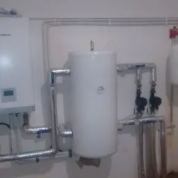 Biały piec gazowy Kaisai, zbiornik wody i naczynie przeponowe połączone rurami w pomieszczeniu kotłowni, widoczne zawory i manometry.