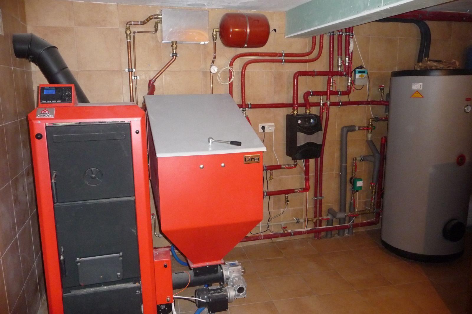 Kotłownia z kotłem na paliwo stałe, zasobnikiem ciepłej wody i licznymi rurami grzewczymi w pomieszczeniu wyłożonym kafelkami.