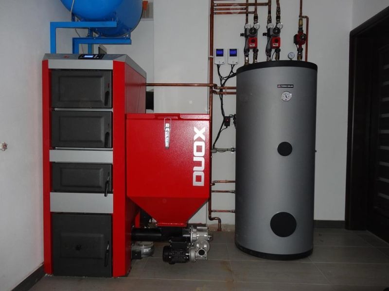 Nowoczesny, automatyczny piec na paliwo stałe DUOX z podajnikiem, zbiornikiem na paliwo, zasobnikiem ciepłej wody użytkowej i instalacją hydrauliczną z rur miedzianych w kotłowni.