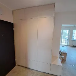 Jasna szafa wnękowa z siedziskiem przy wejściu, widok na otwarte mieszkanie z balkonem w tle.