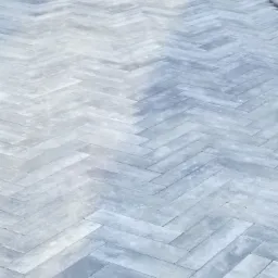 Szara kostka ułożona w jodełkę na podjeździe, widoczne krawędzie i nieułożony fragment oraz kartony w tle.