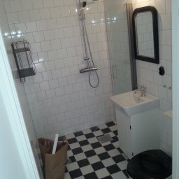 Boike Building Krzysztof Boike - Wykończona łazienka z białą armaturą, kabiną prysznicową i czarno-białą podłogą w szachownicę. Na ścianach białe, prostokątne płytki.