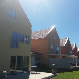 Boike Building Krzysztof Boike - Rząd nowo wybudowanych domów jednorodzinnych z jasnymi elewacjami i czerwonymi dachami, widok z zewnątrz w słoneczny dzień. Widoczne tarasy i elementy zagospodarowania terenu.