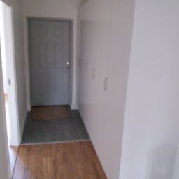 Boike Building Krzysztof Boike - Wnętrze przedpokoju z szarą, zamkniętą ścianą szafy wnękowej z minimalistycznymi uchwytami, szarą podłogą i drewnianą podłogą w dalszej części.