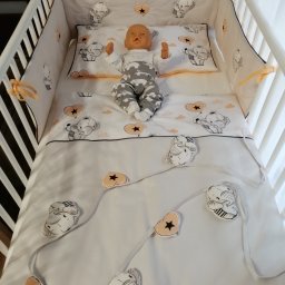 Luli Laj - Białe łóżeczko dziecięce z pościelą w słonie i lalką w środku, widok z góry.