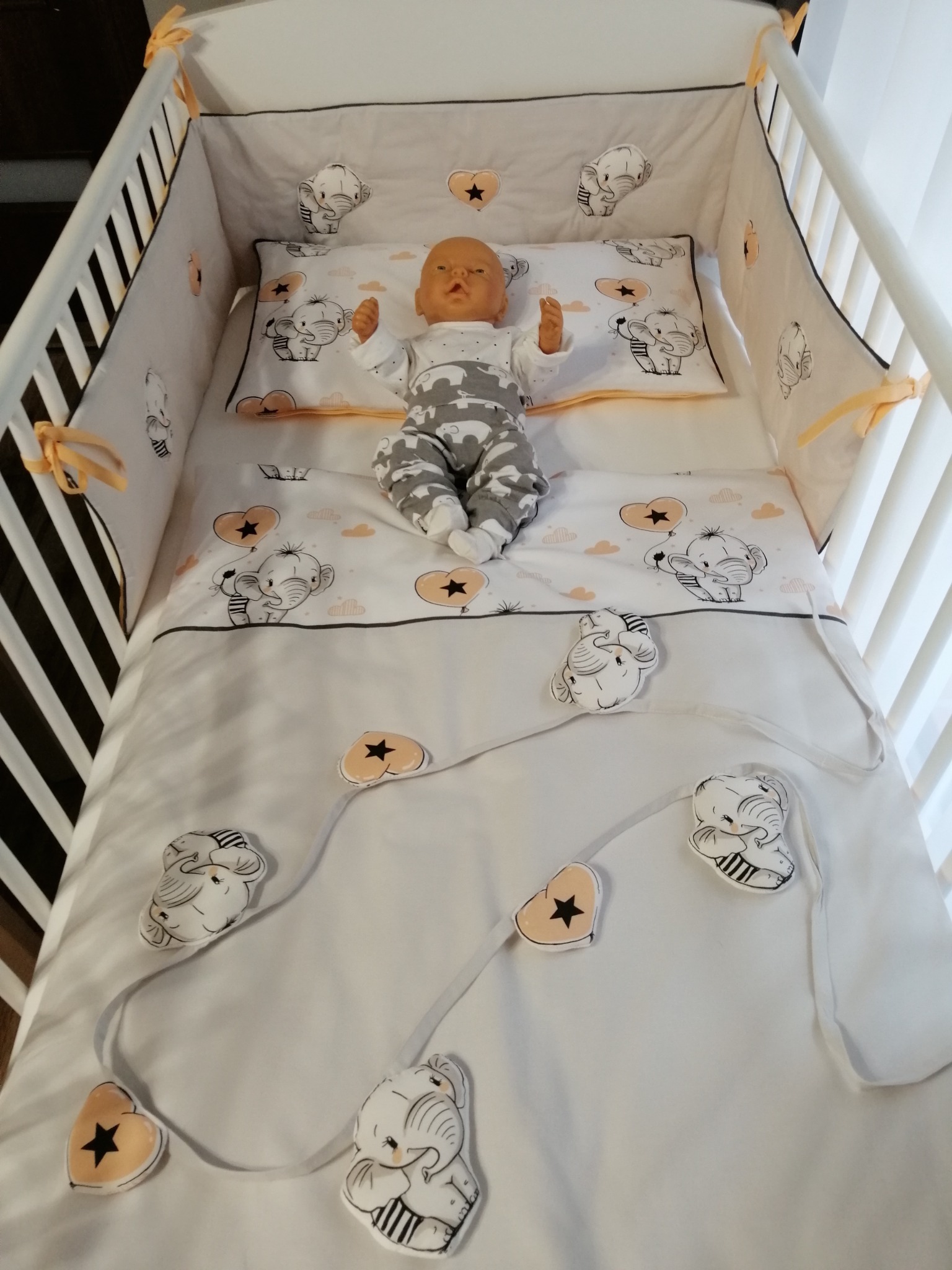 Białe łóżeczko dziecięce z pościelą w słonie i lalką w środku, widok z góry.