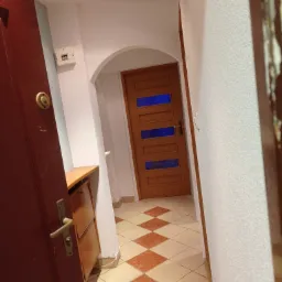 Korytarz po remoncie z nową podłogą z płytek ułożonych w karo, świeżo pomalowanymi ścianami i widoczną szafką na buty.