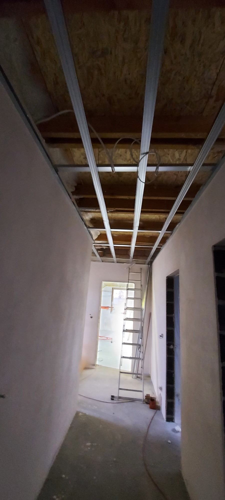 Wnętrze w Jastrzębiu-Zdroju w trakcie remontu: widoczne metalowe profile sufitowe, ściany po nałożeniu gładzi, drabina oparta o ścianę.