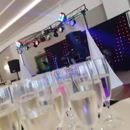 Przygotowany parkiet taneczny z oświetleniem i nagłośnieniem, w tle zastawiony stół z kieliszkami szampana, gotowy na imprezę.