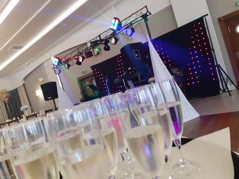 Przygotowany parkiet taneczny z oświetleniem i nagłośnieniem, w tle zastawiony stół z kieliszkami szampana, gotowy na imprezę.